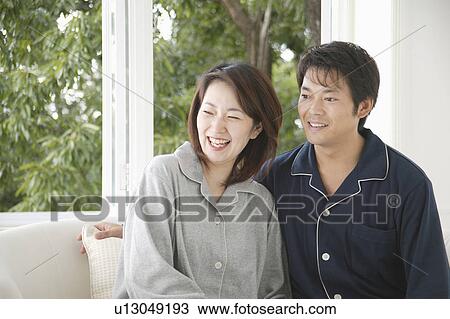 Stock Image - Mid adult couple sitting in sofa. Fotosearch