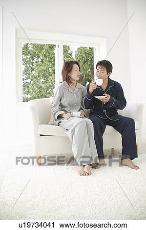 Mid adult couple sitting in sofa with cup in hand View Large Photo Image Stock Image - Mid adult couple sitting in sofa with cup in hand. Fotosearch