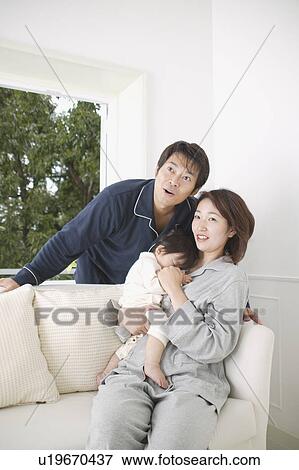 Stock Photo - Mother holding baby girl with father standing behind. Fotosearch