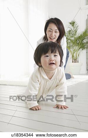 Picture - Baby girl crawling and mother following. Fotosearch