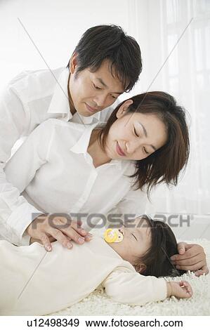 Stock Photo - Baby girl sleeping with parents watching. Fotosearch