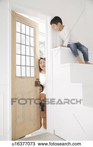 Stock Image - Boy sitting on steps with parents watching behind door. Fotosearch