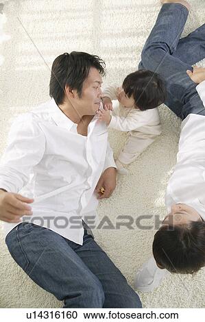 Stock Image - Parents and baby daughter relaxing in living room. Fotosearch