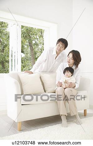 Stock Photo - Parents and a baby girl sitting on a sofa. Fotosearch