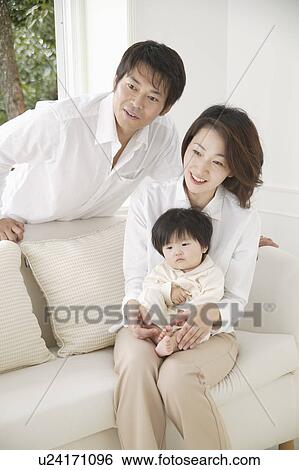 Stock Photograph - Parents and a baby girl sitting on a sofa. Fotosearch