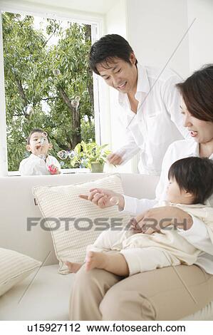 Stock Image - Son playing with bubbles and parents and baby girl watching. Fotosearch