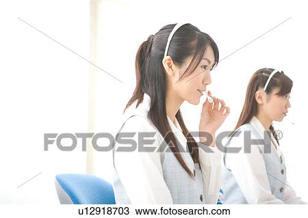 Stock Image - Two young women wearing headsets. Fotosearch