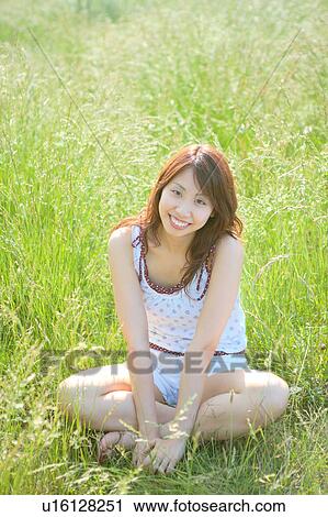 Stock Image - Portrait of young woman sitting in field. Fotosearch