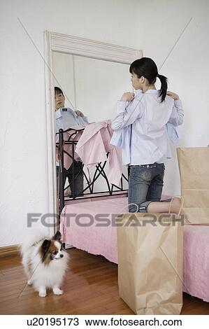 Stock Image - Young woman kneeling on bed and looking in mirror. Fotosearch