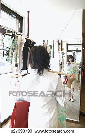 Stock Image - Young woman looking in mirror at clothing store. Fotosearch