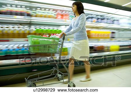 Stock Photo - Young woman shopping at supermarket, blurred motion. Fotosearch
