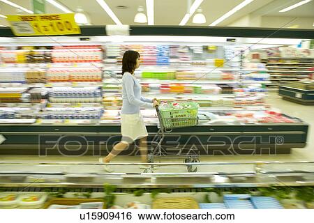 Stock Photograph - Young woman shopping at supermarket, blurred motion. Fotosearch