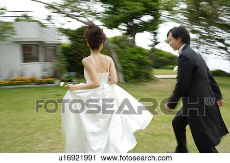 Stock Image - Bride and groom running on lawn, blurred motion. Fotosearch