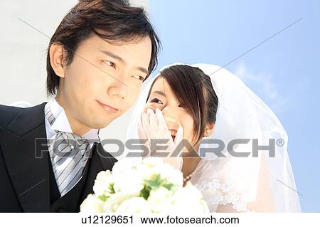 Stock Image - Bride whispering to groom. Fotosearch