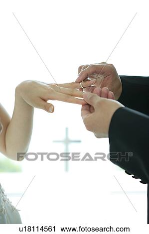 Stock Image - Groom sliding wedding ring onto bride's finger. Fotosearch