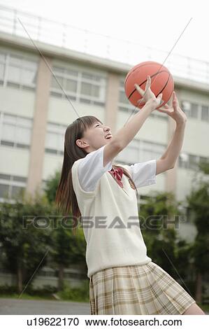 Stock Image - High school girl playing basketball in schoolyard. Fotosearch