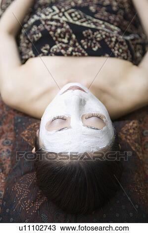 Stock Image - Young woman lying down with facial pack. Fotosearch