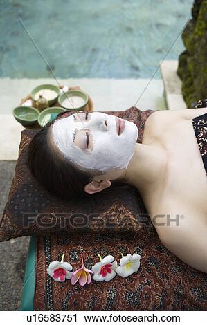 Stock Image - Young woman lying down with facial pack. Fotosearch