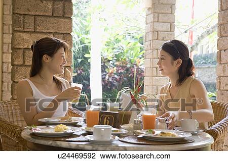 Stock Image - Two young women eating at table. Fotosearch