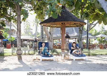 Stock Image - Two young women sitting on deck chairs. Fotosearch