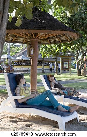 Stock Image - Two young women sitting on deck chairs. Fotosearch