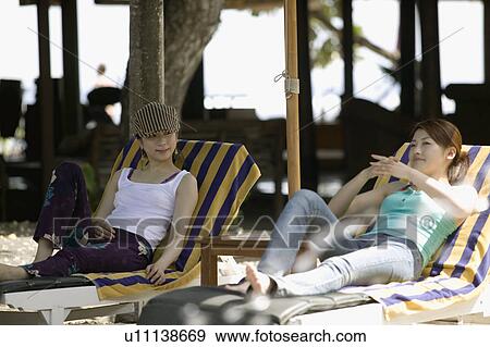 Stock Photo - Two young women sitting on deck chairs. Fotosearch