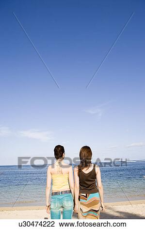 Stock Image - Two young women standing on beach. Fotosearch