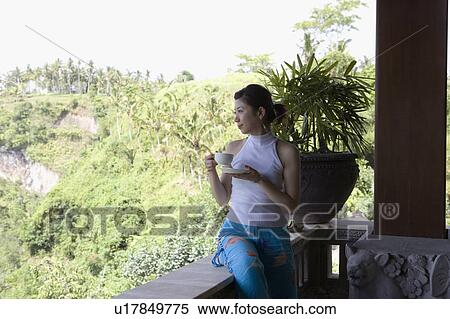 Stock Photography - Young woman having cup of coffee on balcony. Fotosearch