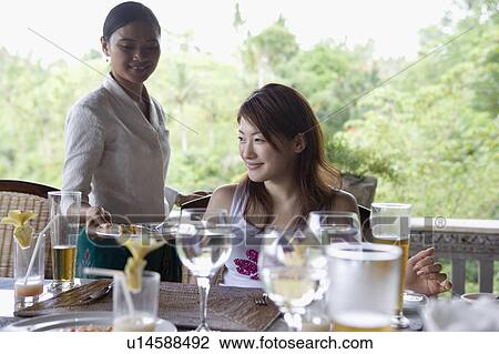 Young woman sitting at table, waitress clearing table View Large Photo Image Stock Image - Young woman sitting at table, waitress clearing table. Fotosearch