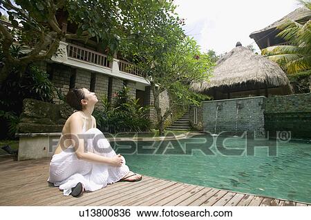 Stock Photograph - Young woman sitting by pool. Fotosearch