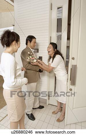Stock Photograph - Mature woman greeting mature couple at front door. Fotosearch