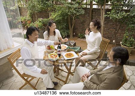 Stock Photograph - Two mature couples sitting at table outside. Fotosearch