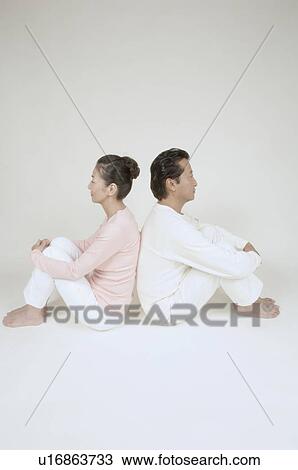 Stock Image - Mature couple sitting back to back, hugging knees. Fotosearch