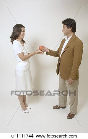 Picture - Mature man giving apple to mature woman. Fotosearch