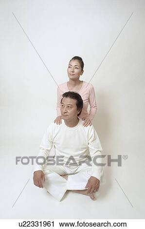 Stock Image - Mature man sitting cross-legged, mature woman behind him. Fotosearch