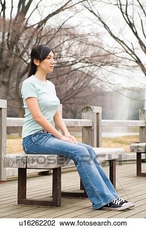 Stock Image - Young woman sitting on bench. Fotosearch