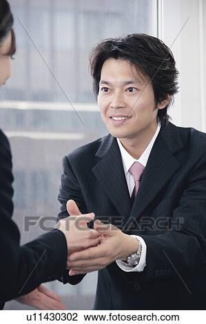 Stock Image - A mid adult man in suit shaking hands. Fotosearch