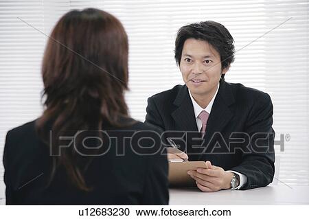 Stock Image - A mid adult man interviewing a young woman. Fotosearch