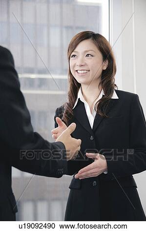 Stock Image - A young woman in suit shaking hands. Fotosearch