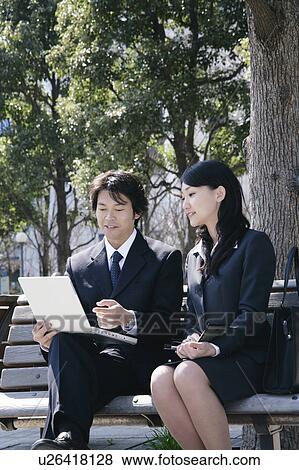 Stock Photo - Young woman and mid adult man sitting on bench. Fotosearch
