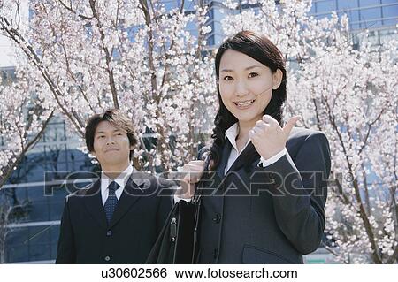 Stock Photograph - Young woman and mid adult man standing in front of cherry blossoms. Fotosearch