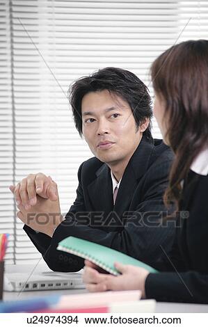 Picture - Young woman and mid adult man talking in office. Fotosearch