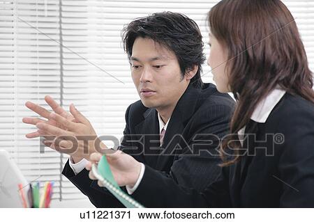 Stock Image - Young woman and mid adult man talking in office. Fotosearch