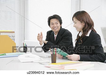 Stock Image - Young woman and mid adult man talking in office. Fotosearch