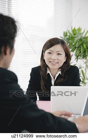 Stock Photo - Young woman and mid adult man talking in office. Fotosearch