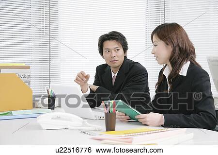 Stock Photograph - Young woman and mid adult man talking in office. Fotosearch