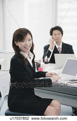Stock Image - Young woman and mid adult man working in office. Fotosearch
