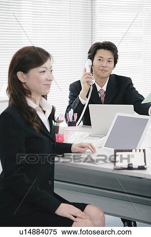 Stock Photography - Young woman and mid adult man working in office. Fotosearch
