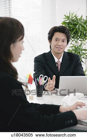 Stock Photography - Young woman and mid adult man working in office. Fotosearch