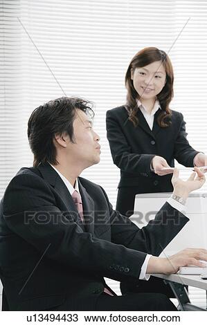 Stock Image - Young woman handing document to her boss. Fotosearch